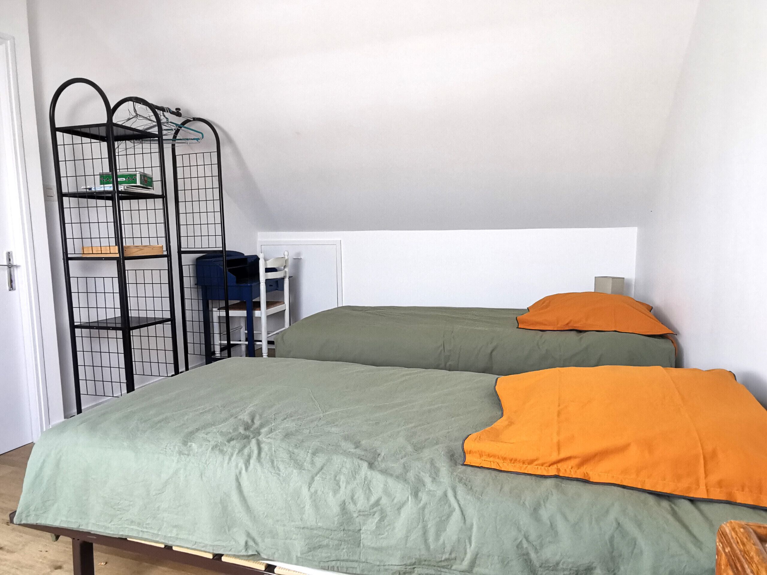 Une chambre avec deux lits, un bureau et une étagère en métal noir.