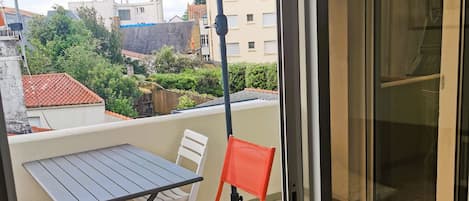 Un balcon avec une table et des chaises, un parasol bleu et une vue sur les bâtiments en arrière-plan.