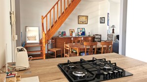 A kitchen with a wooden stove, dining table, chairs, and a staircase. - Désirée Arago  Les Sables (Les Sables-d´Olonne)