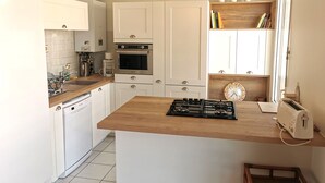 A modern kitchen with white cabinets, a wooden countertop, a gas stove, an oven, and a coffee maker. - Désirée Arago  Les Sables (Les Sables-d´Olonne)