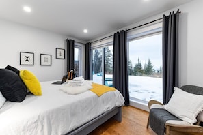 A modern bedroom with a large bed, a chair, and a view of a snowy landscape through a large window.