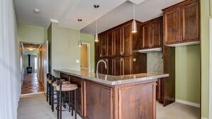 A kitchen with dark wooden cabinets, a granite countertop, and a bar area with stools.