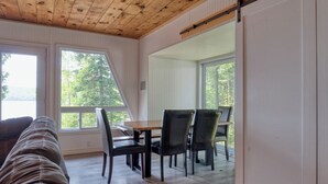 Une pièce chaleureuse avec un plafond en bois, une table à manger avec des chaises et de grandes fenêtres donnant sur la forêt.