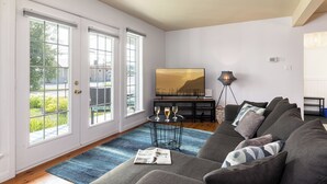 Una sala de estar con un sofá gris, un tapete azul y un cuadro de un paisaje.