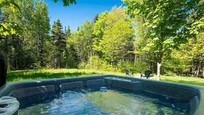 A hot tub surrounded by a forested area with a grassy lawn and a bench.