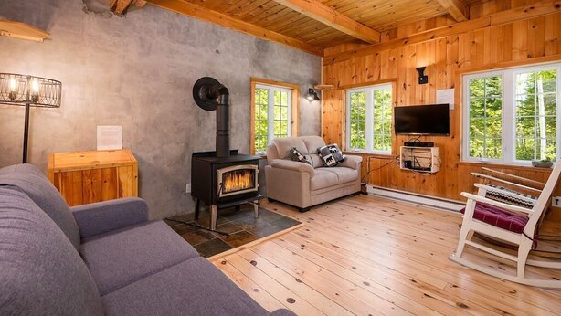 A cozy cabin interior with a fireplace, wooden walls, a sofa, and a rocking chair.