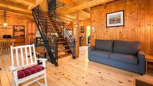A wooden cabin interior with a staircase, a sofa, a bench, and a dining area.