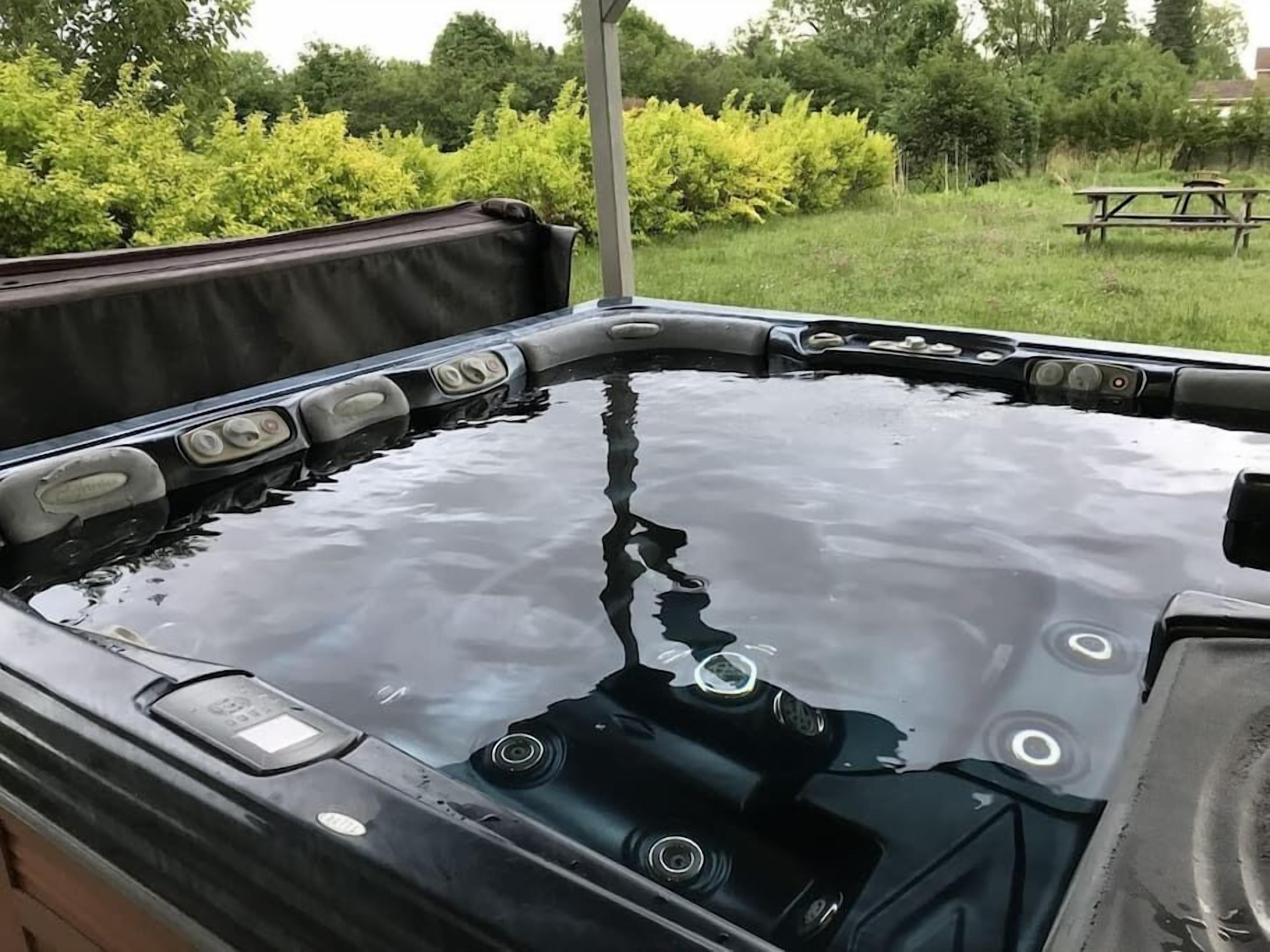 A hot tub with a clear view of the surrounding garden and a picnic table in the background.