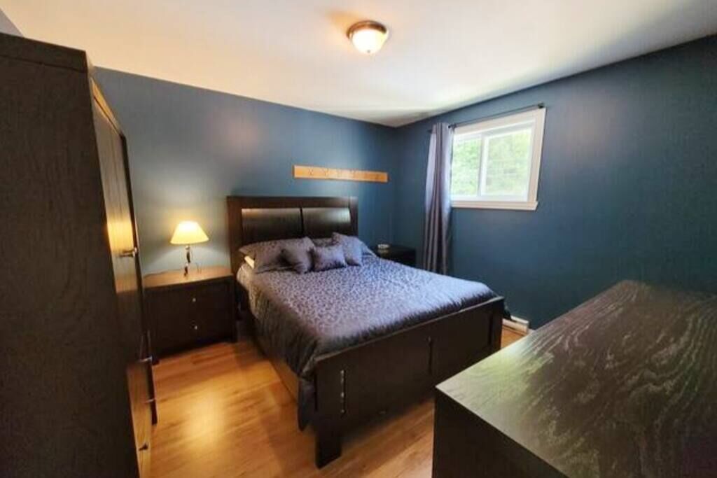 A bedroom with a bed, bedside table, lamp, and a window.