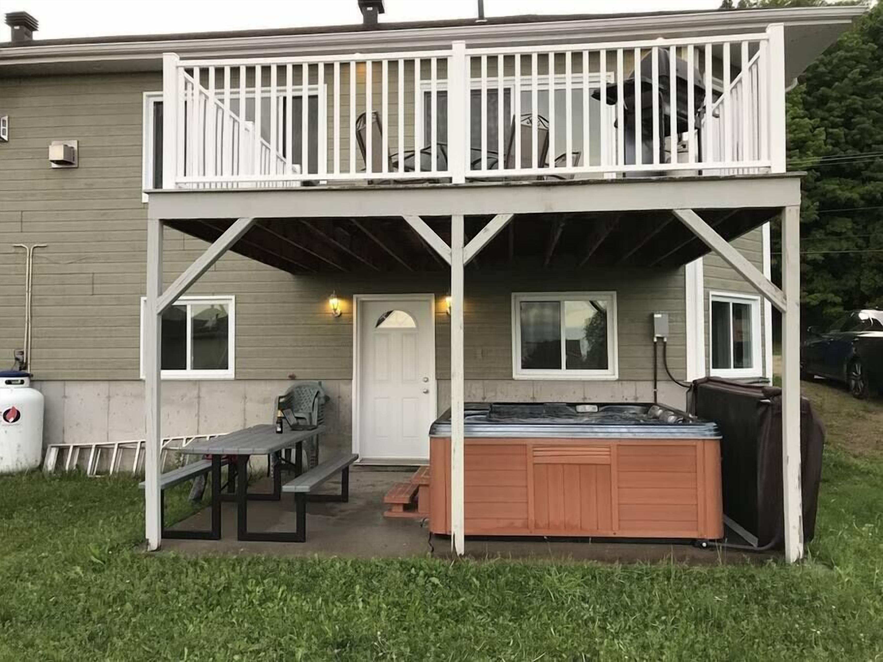 Un bâtiment à deux étages doté d’un balcon, d’un jacuzzi et d’un espace patio avec une table et des chaises.