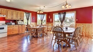 Zona pranzo con sedie e tavolo in legno, cucina con mobili in legno e ampie finestre con tende.