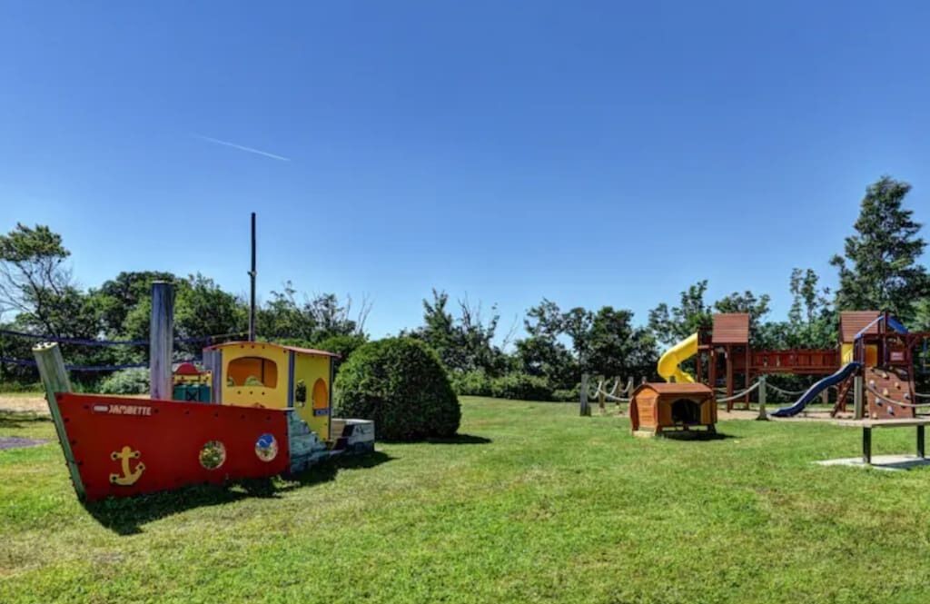 A playground with slides and climbing structures, a small boat-shaped playhouse, and a wooden cabin.
