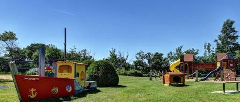 A playground with slides and climbing structures, a small boat-shaped playhouse, and a wooden cabin.