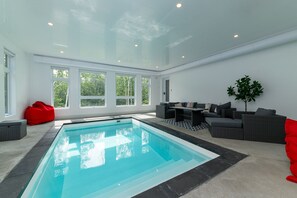 An indoor swimming pool with a modern design, surrounded by a seating area with sofas and a dining table. - Hôtel à la maison - Le Distinction, piscine et spa (Petite-Rivière-Saint-François)