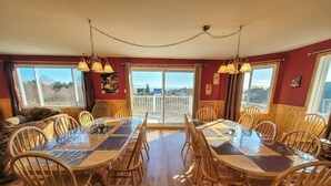 A dining area with a large table and chairs, wooden walls, and large windows with a view. - Hôtel à la maison - La Maison Elsa, fleuve et ski (Petite-Rivière-Saint-François)