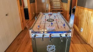 A foosball table in a room with wooden flooring and walls, a staircase, and a door. - Hôtel à la maison - La Maison Elsa, fleuve et ski (Petite-Rivière-Saint-François)