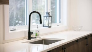 Una cocina moderna con un grifo negro, un tazón de vidrio transparente y una encimera blanca.