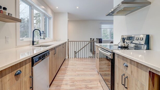 Una cocina moderna con armarios de madera, lavavajillas, estufa y ventana que aporta luz natural.