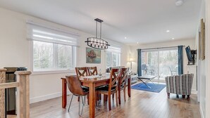 Un comedor amplio con mesa y sillas de madera, ventanas grandes y una lámpara moderna.