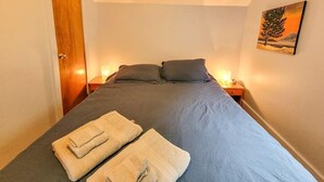 Een slaapkamer met een bed, twee nachtkastjes, een deur en een schilderij aan de muur.