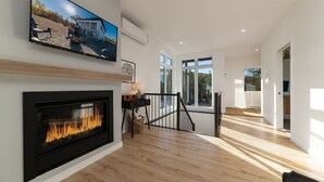 Ein modernes Wohnzimmer mit Kamin, einem an der Wand befestigten Fernseher und einer Treppe, die zu einer weiteren Ebene führt.