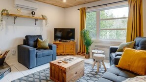 Ein gemütliches Wohnzimmer mit Holzboden, einem Fernseher auf einem Holzschrank, zwei Sofas, einem Couchtisch und einem Fenster mit Vorhängen.