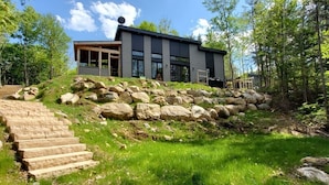 A modern house with a stone staircase leading up to a wooden deck. - Hôtel à la maison - Chalet la Carpe, Spa et Lac (Chertsey)