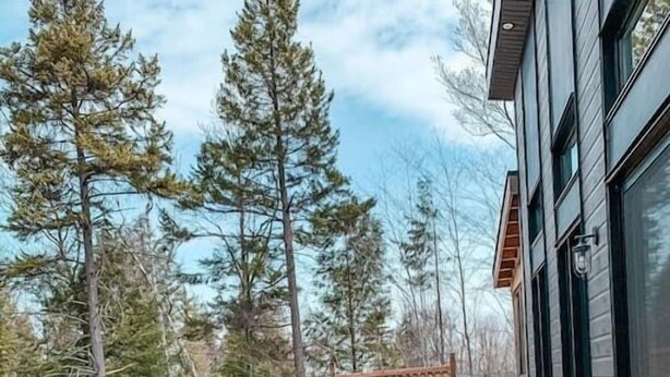 A wooden deck with a hot tub, two wicker chairs, and a view of trees. - Hôtel à la maison - Chalet la Carpe, Spa et Lac (Chertsey)