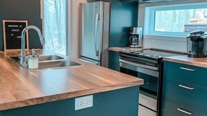 A modern kitchen with dark cabinetry, a stainless steel refrigerator, a built-in oven, and a wooden countertop. - Hôtel à la maison - Chalet la Carpe, Spa et Lac (Chertsey)