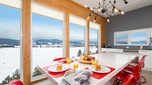 A modern dining area with a large table, red chairs, and a view of a snowy landscape. - Hôtel à la maison - Panache, spa et fleuve (Baie-Saint-Paul)