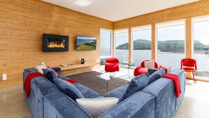A modern living room with a fireplace, large windows overlooking a lake, and a cozy seating area. - Hôtel à la maison - Panache, spa et fleuve (Baie-Saint-Paul)