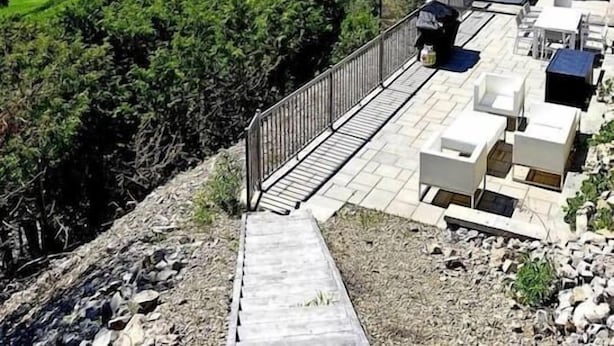 A modern building with a terrace and outdoor seating area, overlooking a green landscape and distant hills. - Hôtel à la maison - Panache, spa et fleuve (Baie-Saint-Paul)