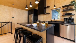 Una cocina moderna con paredes de madera, una isla central con taburetes, electrodomésticos de acero inoxidable e iluminación colgante.