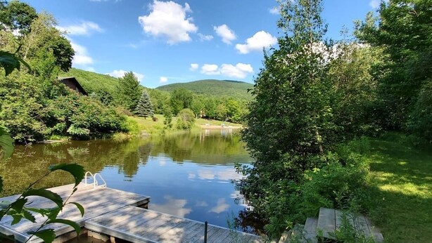 A serene lakeside setting with a dock extending into the water, surrounded by lush greenery and hills in the background. - Hôtel à la maison - L'Éphémère, Nature et Lac! (Sutton)
