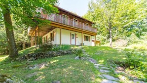 A two-story house with a balcony, surrounded by a stone wall and a stone pathway leading to the entrance. - Hôtel à la maison - L'Éphémère, Nature et Lac! (Sutton)