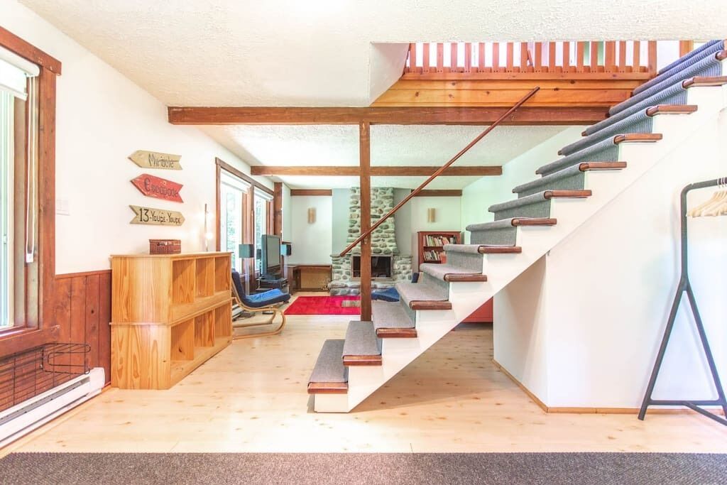 A staircase leading to a loft area with a wooden railing, a stone wall, and a television in the background.