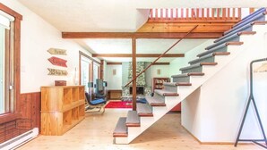 A staircase leading to a loft area with a wooden railing, a stone wall, and a television in the background. - Hôtel à la maison - L'Éphémère, Nature et Lac! (Sutton)