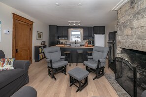 A modern kitchen with dark cabinets, a central island, and a stone fireplace.