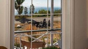 A view through a window with a white frame, overlooking a road with a parked vehicle, a table, and chairs outside.