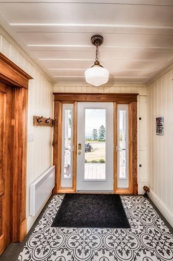 A hallway with a wooden door, a black doormat, patterned floor tiles, and a ceiling light fixture.