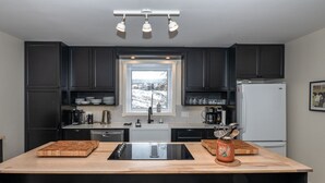 A modern kitchen with dark cabinets, a central island with a sink, and a window above the sink.