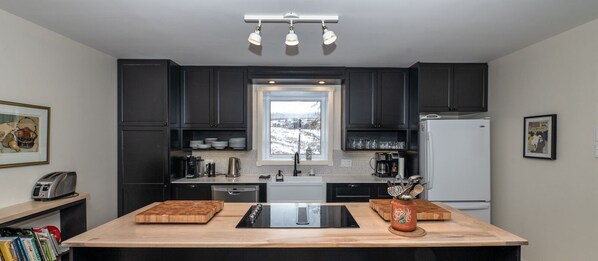 A modern kitchen with dark cabinets, a central island with a sink, and a window above the sink.