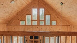 A wooden interior with a high ceiling, triangular roof, and multiple windows.