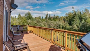 A wooden deck with a railing, outdoor furniture, and a grill.