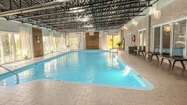 Una piscina interior con paredes de vidrio transparente, suelo de baldosas y estructura de techo metálica.
