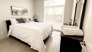 Un dormitorio con cama, mesita de noche, lámpara y ventana con persianas.