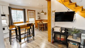 Eine moderne Küche mit Holzboden, einem Essbereich mit Holztisch und -stühlen, einem schwarzen Schrank und einem an der Wand montierten Fernseher sowie einer Treppe mit Holzstufen.