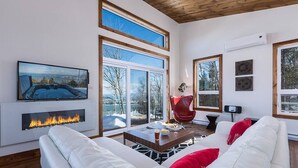 A modern living room with a fireplace, large windows, and a cozy seating area. - Hôtel à la maison - L'Horizon, spa et fleuve (Les Éboulements)