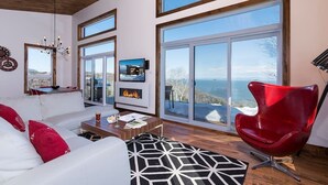 A modern living room with a white sofa, red chair, and a fireplace. - Hôtel à la maison - L'Horizon, spa et fleuve (Les Éboulements)