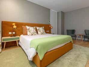Een moderne hotelkamer met een groot bed, twee nachtkastjes met lampen, een groene plaid en twee stoelen.